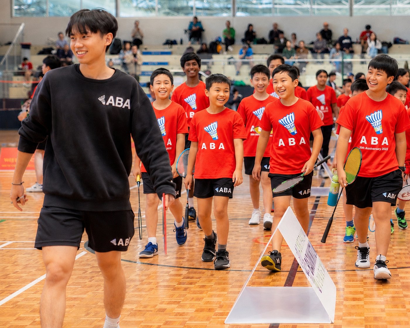 An ABA coach leading a large group of junior players onto the court at an academy event